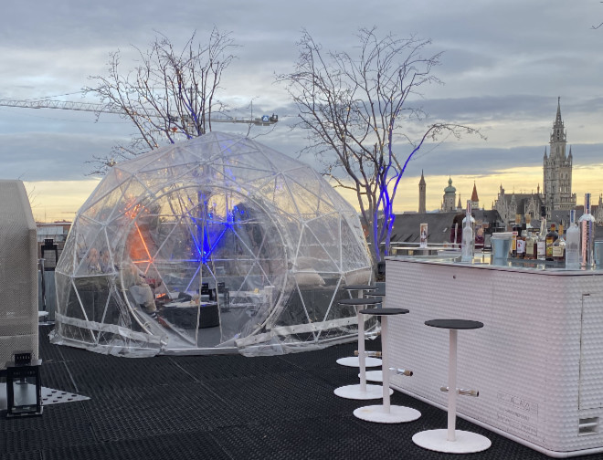 Die Outdoor-Bar präsentiert sich mit windgeschützten Sitzbänken, Feuerstellen und einem Iglu Pavillon über den Dächern der Stadt München