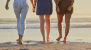 Friends, girl group and back at beach for walk on vacation, holiday or summer travel together in sunshine. Legs, holding hands and women walking to relax in ocean sand, sea or water in solidarity