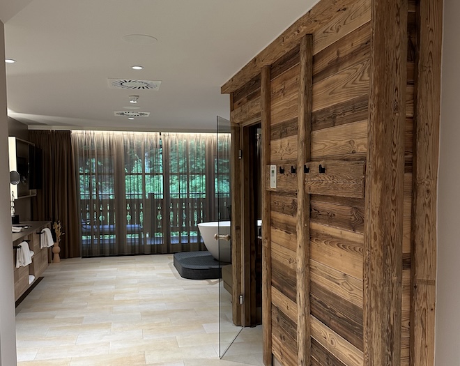 Diese stilvolle Kombination aus Altholz-Sauna, Naturstein und freistehender Badewanne schafft einen privaten Spa-Bereich mit alpinem Flair – ideal für urbane Rückzugsorte.