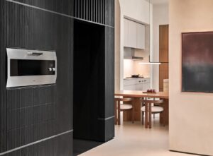Gaggenau Backofen EB 333 in einer dunklen Schrankwand neben einer hellen Küche mit Esstisch.