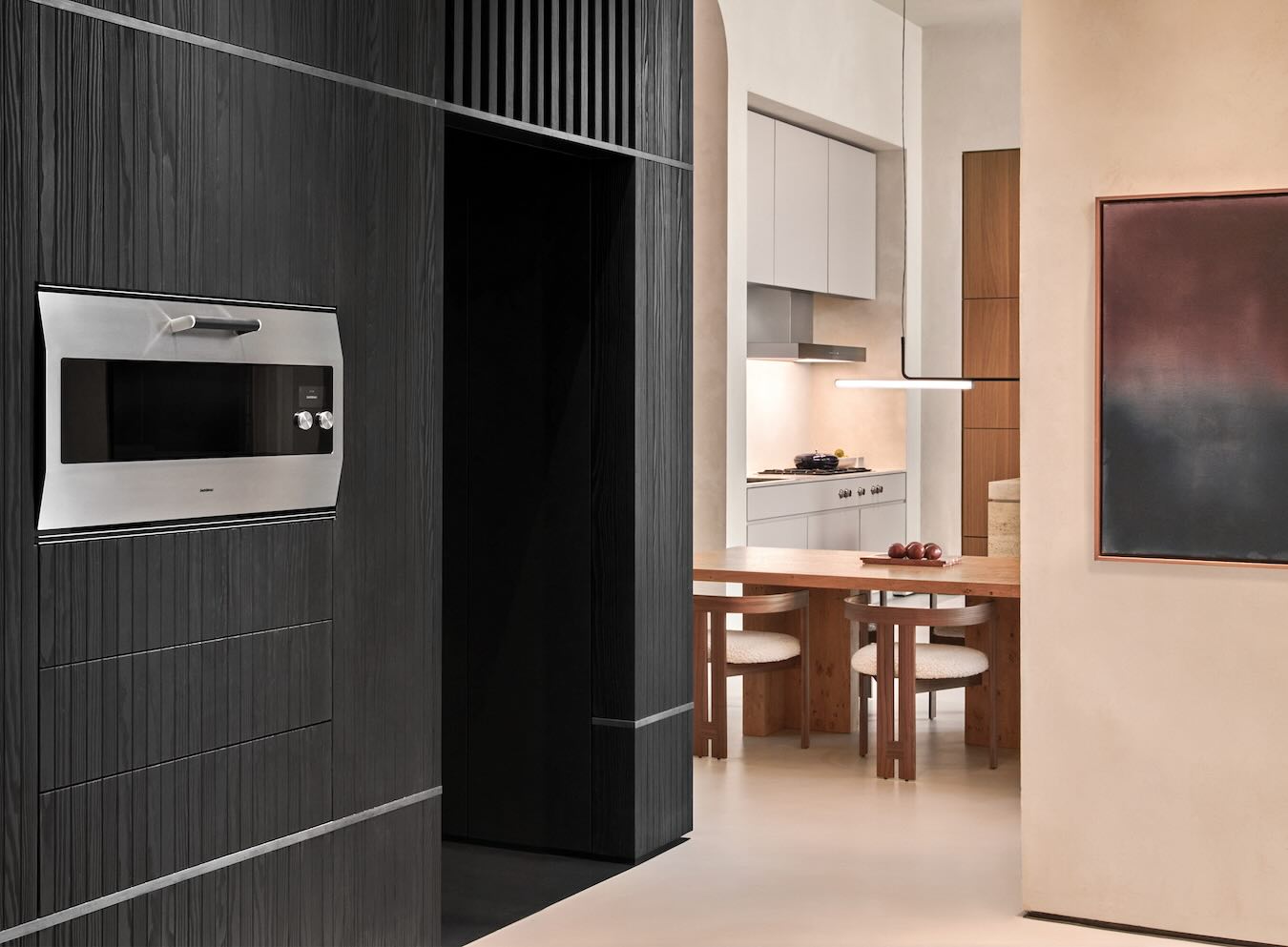 Gaggenau Backofen EB 333 in einer dunklen Schrankwand neben einer hellen Küche mit Esstisch.