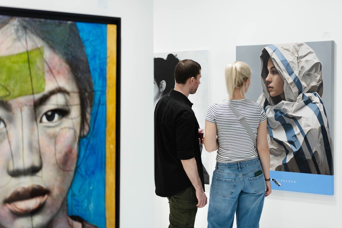 Zwei Besucher betrachten großformatige Frauenporträts auf der ARTMUC Kunstmesse in München.