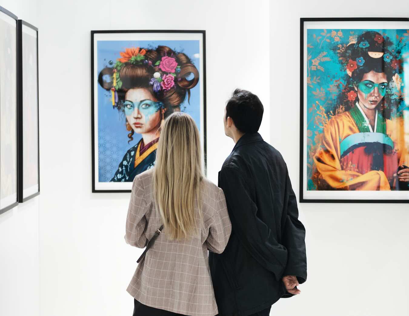 Zwei Besucher betrachten auf der ARTMUC farbenfrohe Frauenporträts mit floralem Haarschmuck und asiatisch inspirierten Gewändern.