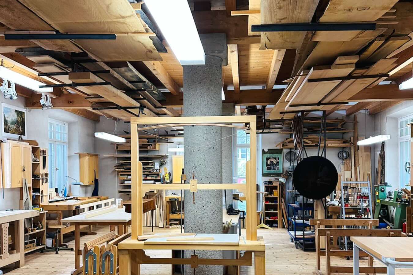 Werkstatt des Greifenberger Instituts mit Werkbänken, Werkzeugen und unter der Decke gelagerten Holzbrettern. Der helle Raum wird auch für Konzerte genutzt.