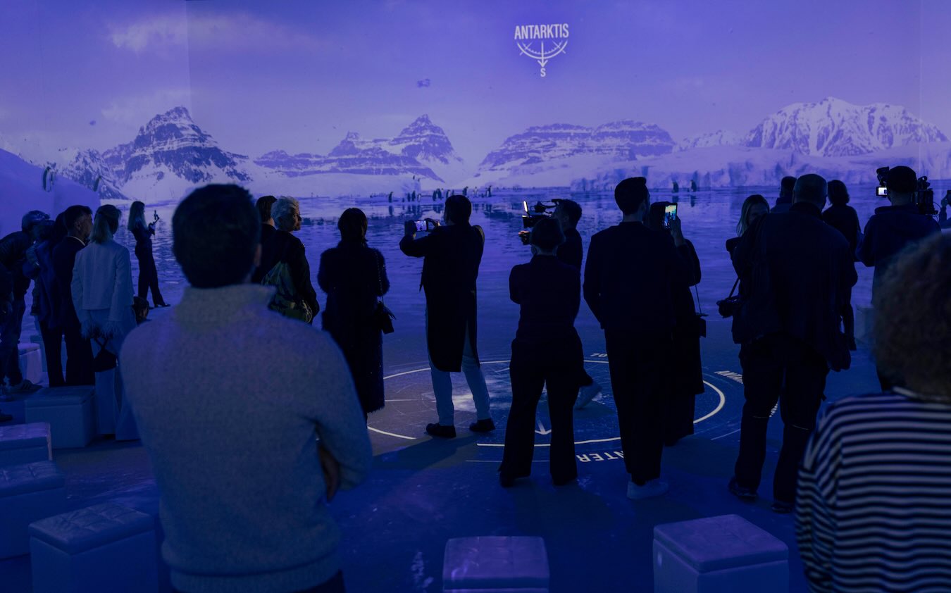 Besucher betrachten eine raumfüllende Projektion mit antarktischen Bergen, Eis und Pinguinen in der Ausstellung „Polarwelten“ in München.