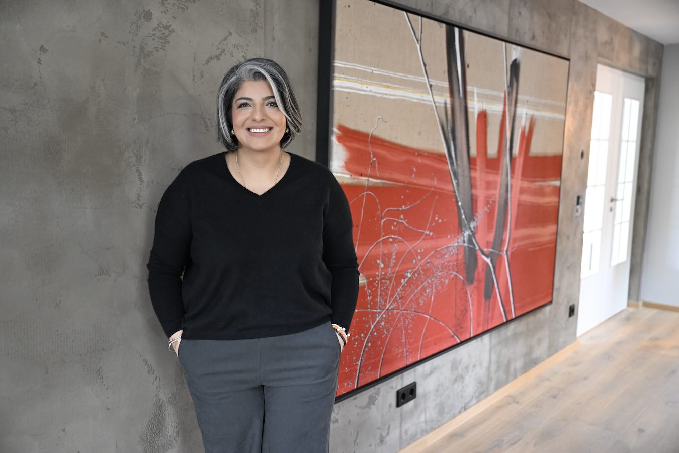 Sahar Essmann, CEO von Sophia Lauton 360° Crafted, in ihrem Privathaus vor einer grauen Wand mit großformatigem abstraktem Kunstwerk in Rot.