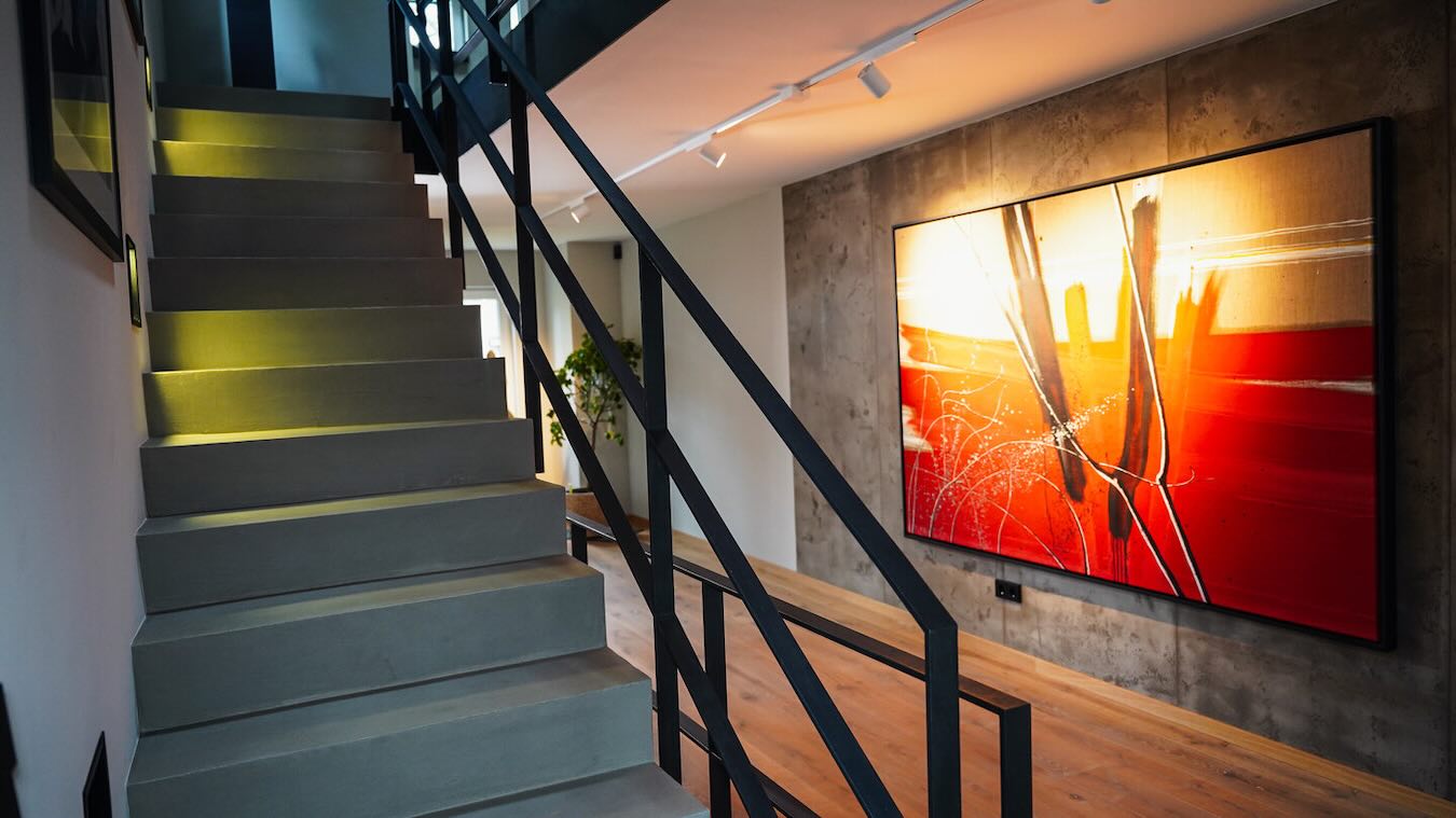 Graue Treppe mit schwarzem Metallgeländer neben Holzboden und großformatigem Kunstwerk in Rot und Gelb im Privathaus von Sahar Essmann.