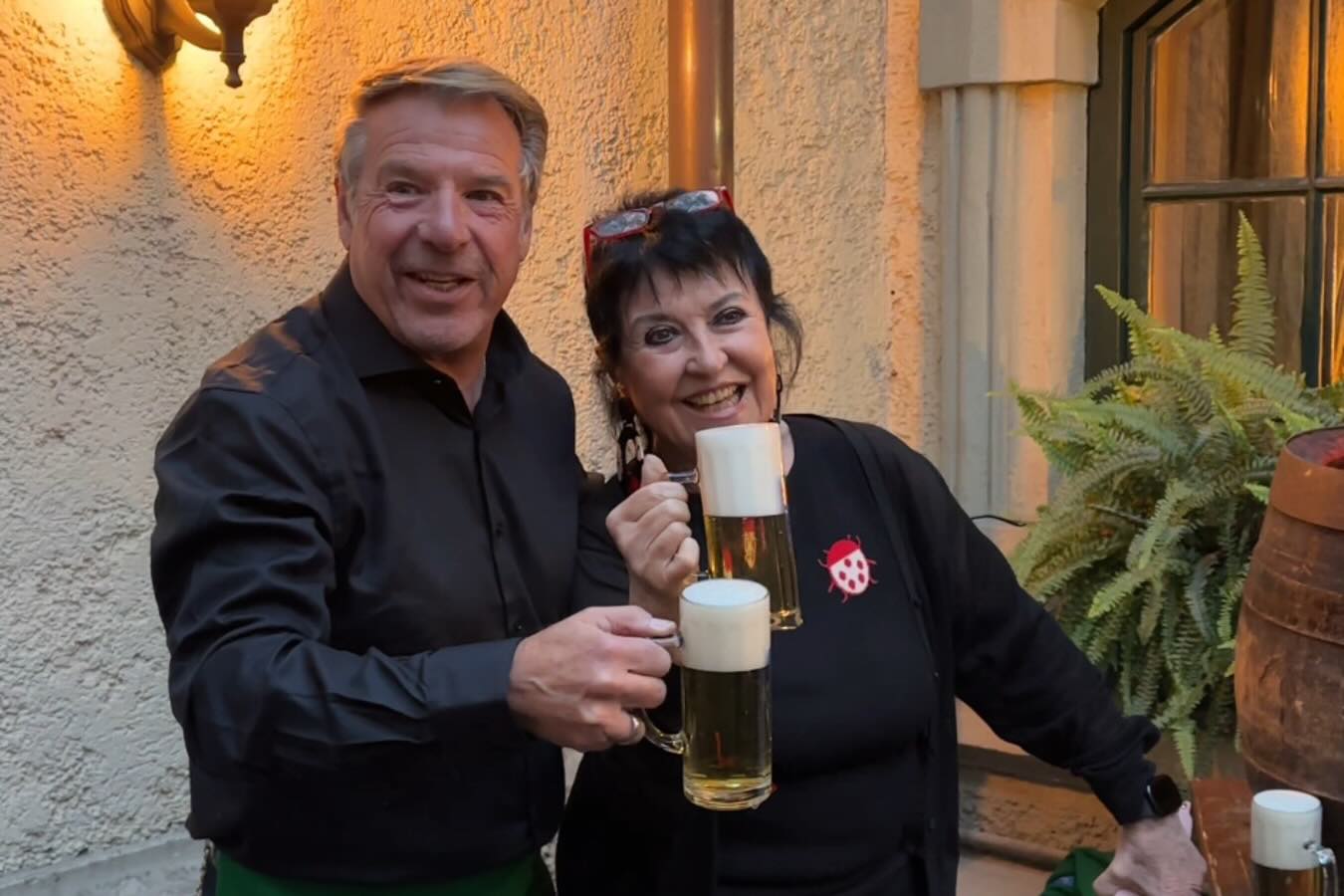 Patrick Lindner und Uschi Ackermann halten nach dem Anzapfen gefüllte Bierkrüge neben dem Fass und lächeln in die Kamera.